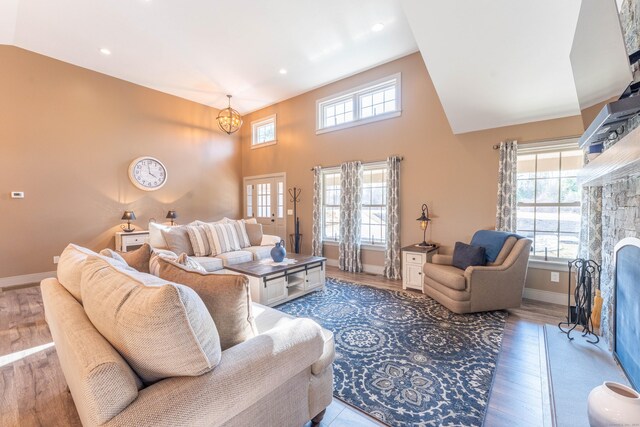 living room with a fireplace with flush hearth, wood finished floors, high vaulted ceiling, and baseboards