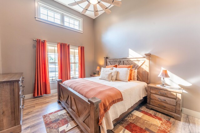 bedroom with a towering ceiling, light wood-style floors, baseboards, and a ceiling fan