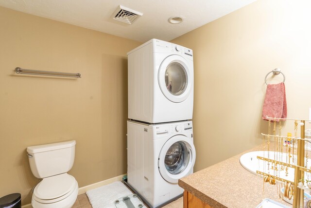 laundry area featuring laundry area, visible vents, light tile patterned flooring, baseboards, and stacked washer / drying machine