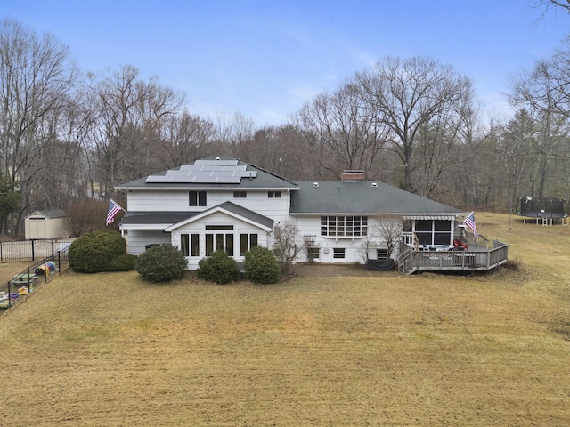 rear view of property with a lawn, a trampoline, a deck, and solar panels