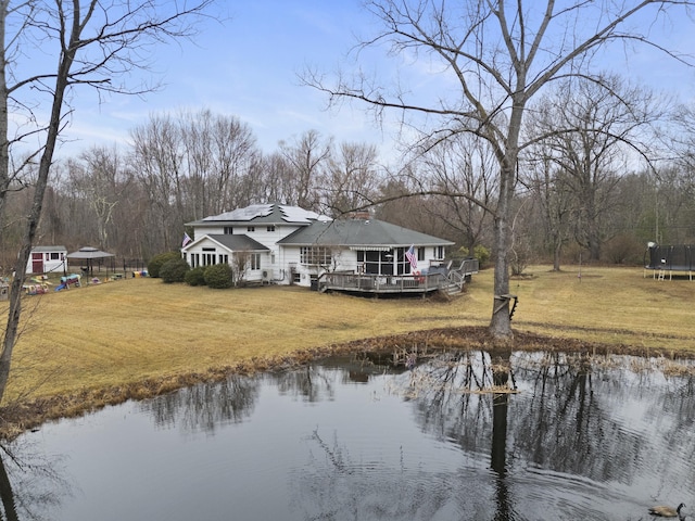 rear view of house with a deck with water view, a trampoline, and a yard