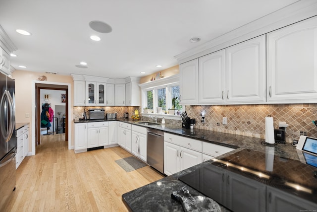 kitchen with appliances with stainless steel finishes, tasteful backsplash, a sink, white cabinets, and light wood finished floors