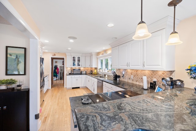 kitchen featuring white cabinets, a sink, light wood finished floors, dark stone countertops, and backsplash