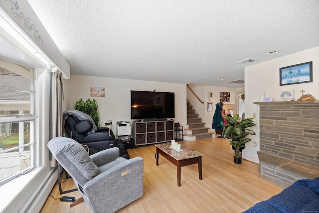living area with stairs, a textured ceiling, visible vents, and light wood finished floors
