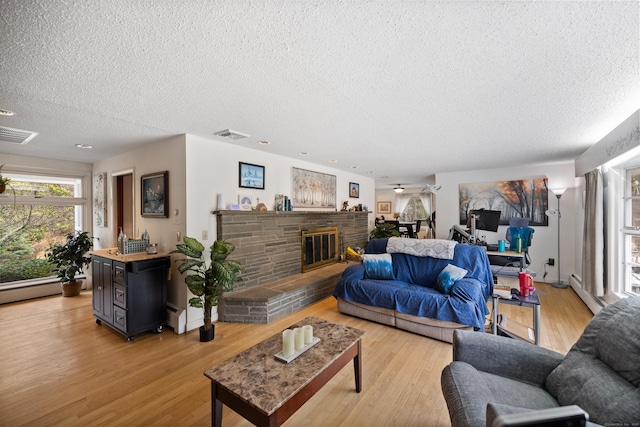 living area featuring visible vents, a textured ceiling, a glass covered fireplace, and light wood-style floors