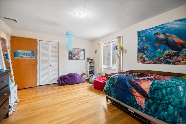 bedroom with visible vents, wood finished floors, and a closet