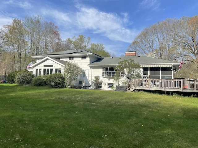 back of house with a chimney, a deck, a sunroom, roof mounted solar panels, and a yard