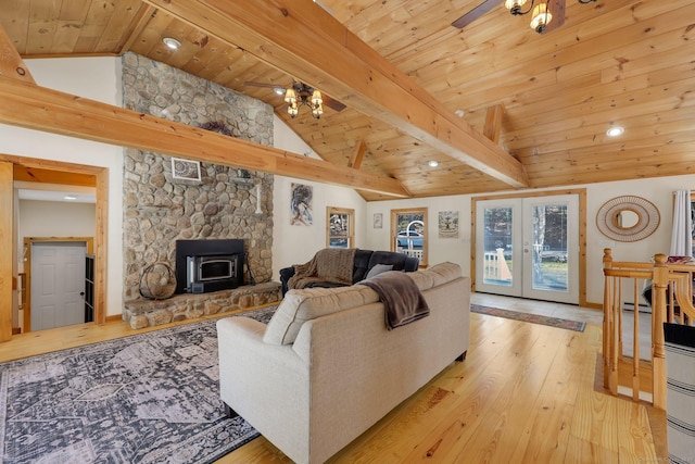 living room with beamed ceiling, light wood-style floors, a wood stove, french doors, and wood ceiling