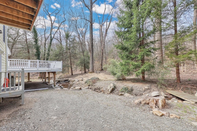 view of yard with dirt driveway, a wooden deck, and a carport