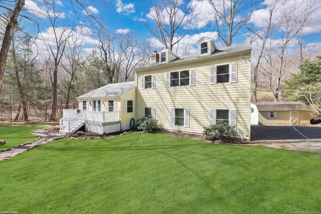 rear view of property featuring a wooden deck, an outdoor structure, aphalt driveway, and a lawn