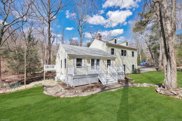 back of property with a deck, a shingled roof, a yard, and a chimney