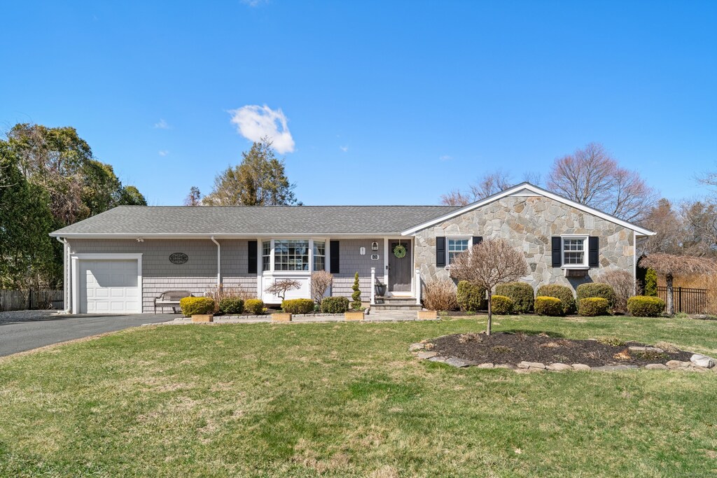 ranch-style house featuring driveway, stone siding, fence, a front lawn, and a garage