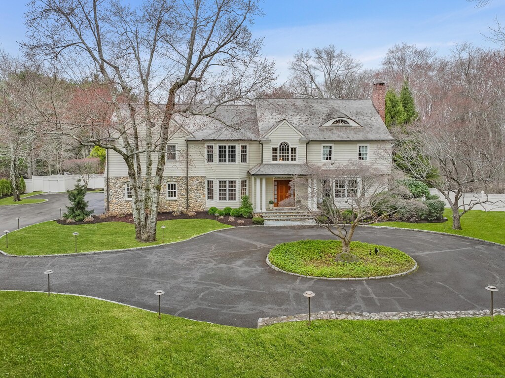 view of front of property with curved driveway, fence, stone siding, a front lawn, and a chimney