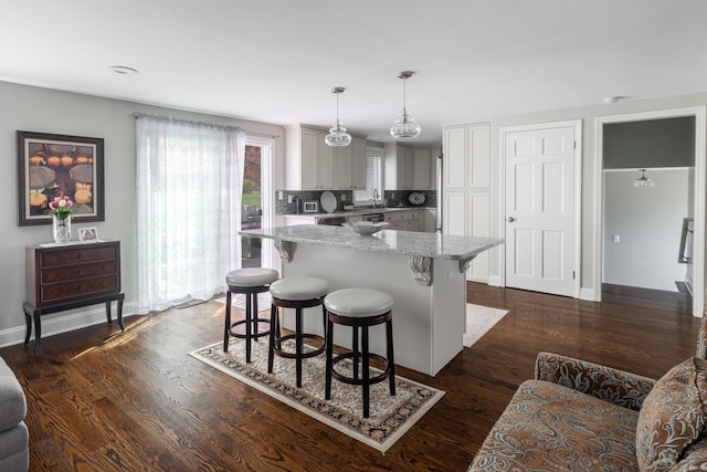 kitchen with light stone countertops, decorative backsplash, a kitchen bar, decorative light fixtures, and baseboards
