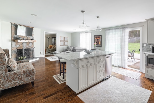 kitchen featuring stainless steel microwave, a stone fireplace, dark wood-style floors, open floor plan, and a kitchen breakfast bar