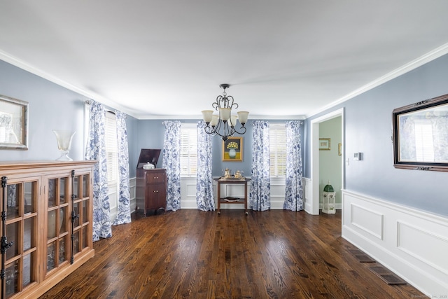 dining space featuring wood finished floors, a decorative wall, ornamental molding, a wainscoted wall, and a notable chandelier
