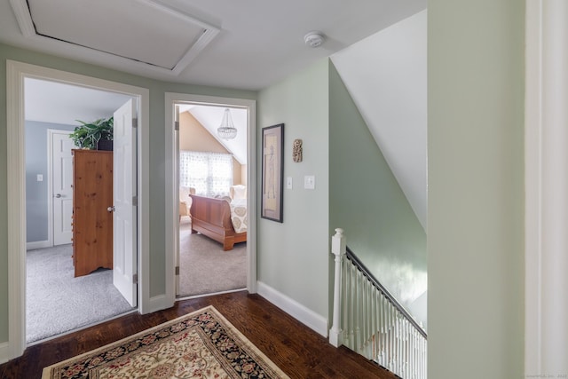corridor featuring an upstairs landing, dark wood-type flooring, attic access, and baseboards