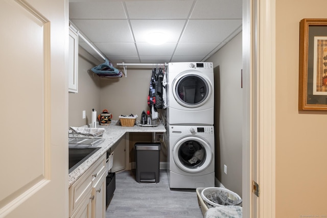 laundry room featuring stacked washer / dryer, light wood finished floors, and a sink