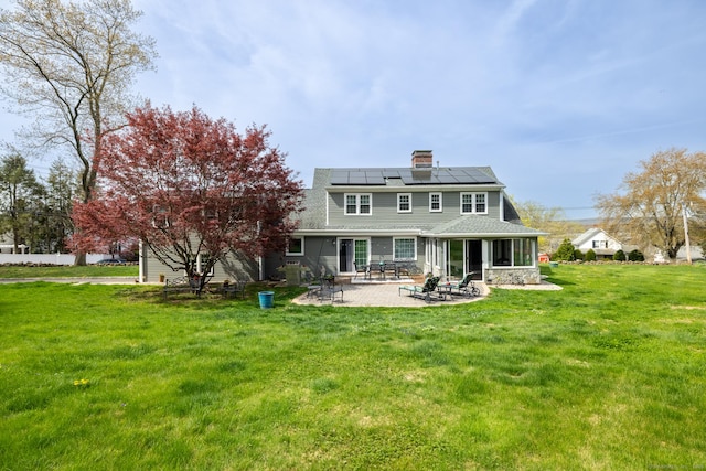 back of property featuring a lawn, a chimney, a patio, and solar panels