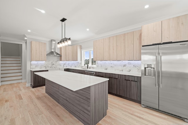 kitchen featuring a sink, appliances with stainless steel finishes, light brown cabinetry, wall chimney exhaust hood, and modern cabinets