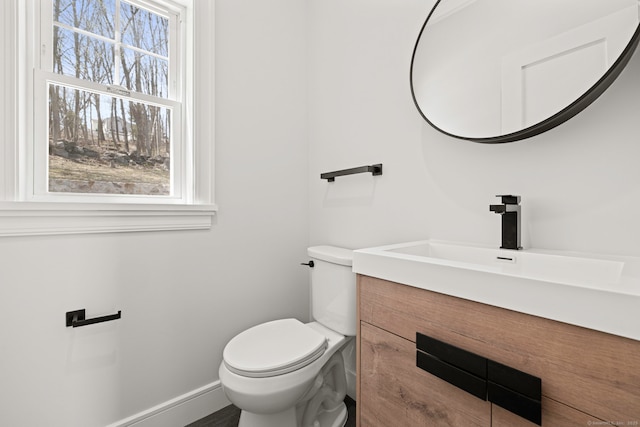 half bath featuring a wealth of natural light, vanity, toilet, and baseboards