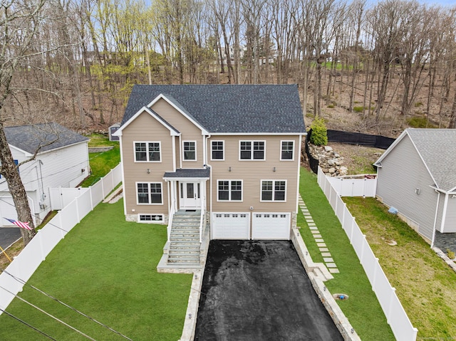 view of front facade with a front lawn, a garage, a shingled roof, a fenced backyard, and aphalt driveway