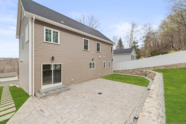 back of property with a lawn, fence, roof with shingles, and a patio