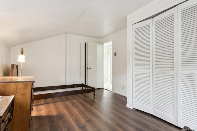 unfurnished bedroom featuring a closet, baseboards, lofted ceiling, and dark wood-style floors