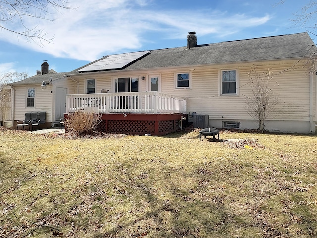 back of property featuring a chimney, central AC unit, an outdoor fire pit, a yard, and a deck