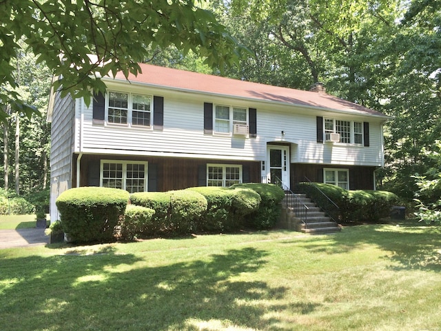 raised ranch with a front yard and cooling unit