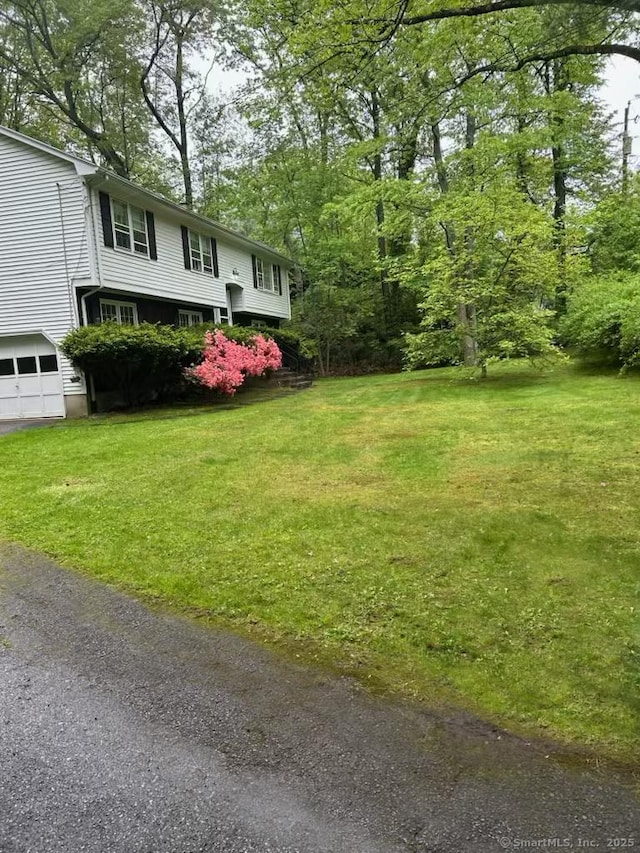 view of green lawn featuring a garage and driveway