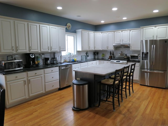 kitchen with appliances with stainless steel finishes, under cabinet range hood, white cabinetry, a sink, and light wood-style floors