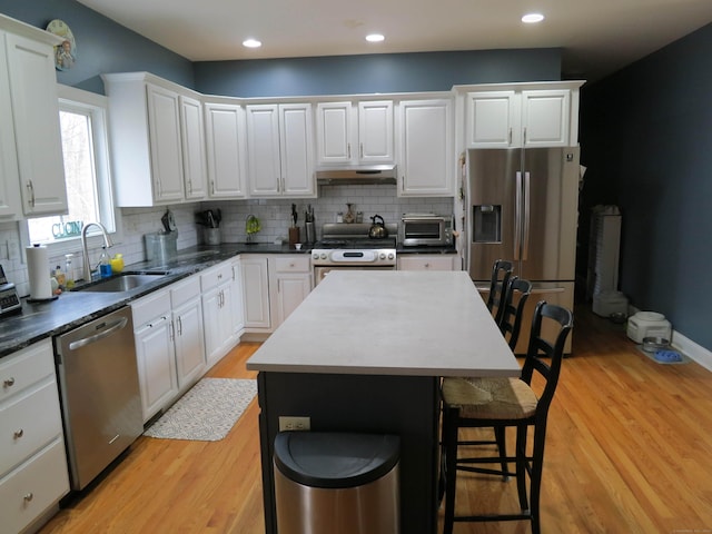 kitchen with light wood-style flooring, a breakfast bar, appliances with stainless steel finishes, under cabinet range hood, and a sink