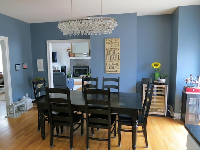 dining room featuring an inviting chandelier, light wood-style flooring, wine cooler, and a fireplace