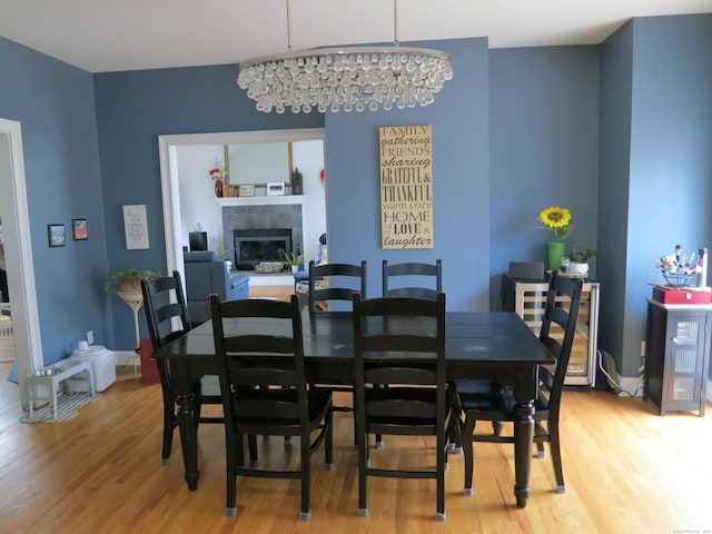 dining space with a tile fireplace, a notable chandelier, and light wood-type flooring