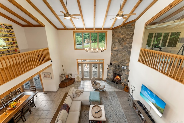 living area featuring stone finish floor, beamed ceiling, a fireplace, high vaulted ceiling, and ceiling fan with notable chandelier