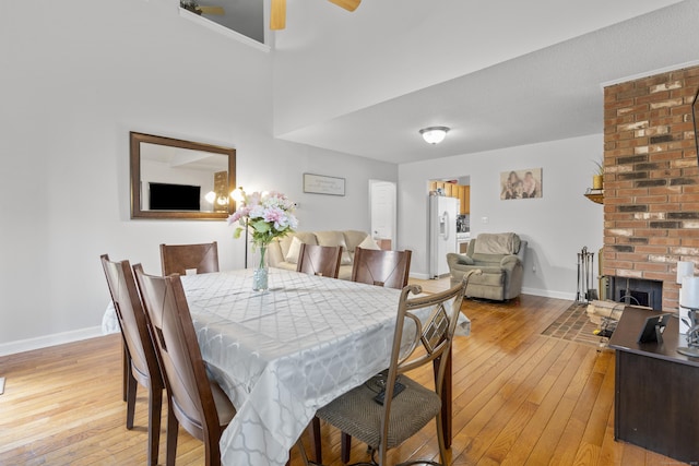dining space featuring a brick fireplace, light wood-style floors, baseboards, and ceiling fan