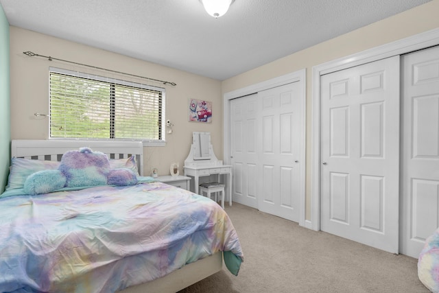 bedroom featuring a textured ceiling, light colored carpet, and multiple closets