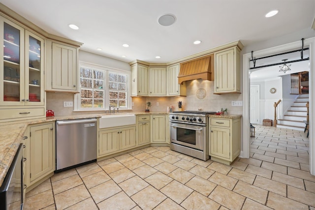 kitchen with custom exhaust hood, tasteful backsplash, a sink, appliances with stainless steel finishes, and cream cabinetry