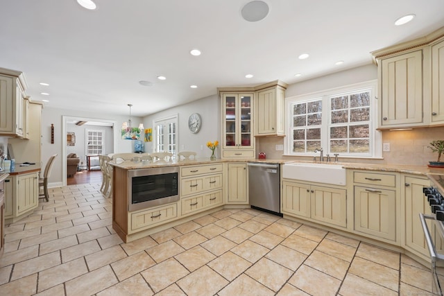 kitchen featuring a peninsula, cream cabinets, built in microwave, dishwasher, and a sink