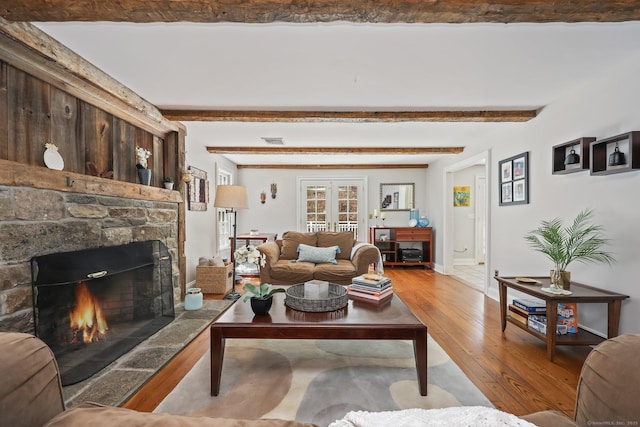 living area featuring light wood-style floors, a fireplace, visible vents, baseboards, and beam ceiling