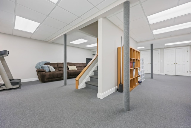 finished below grade area featuring carpet flooring, baseboards, a drop ceiling, and stairs