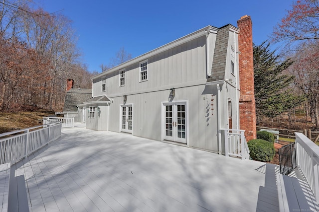 rear view of house with a deck, french doors, a chimney, and a shingled roof