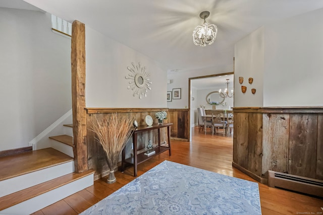 entrance foyer with stairway, a notable chandelier, a baseboard radiator, and wood finished floors