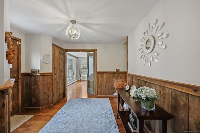 hall with wooden walls, an inviting chandelier, a wainscoted wall, and wood finished floors