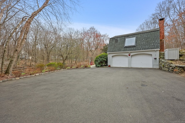 view of side of property featuring roof with shingles, a chimney, and aphalt driveway