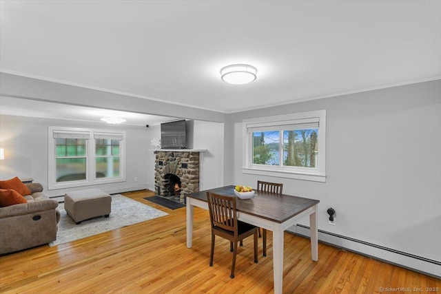 dining room featuring a fireplace, light wood-type flooring, a baseboard heating unit, and ornamental molding