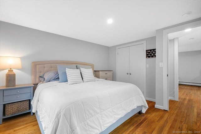 bedroom with wood finished floors, a baseboard heating unit, a closet, and baseboards