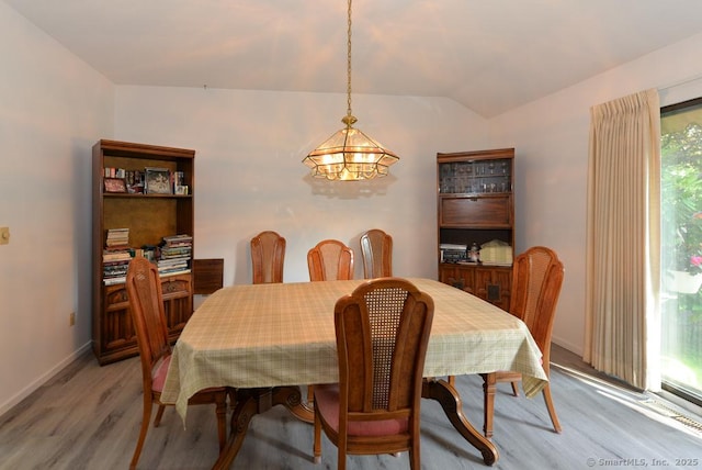 dining space with baseboards, lofted ceiling, light wood-style flooring, and a chandelier