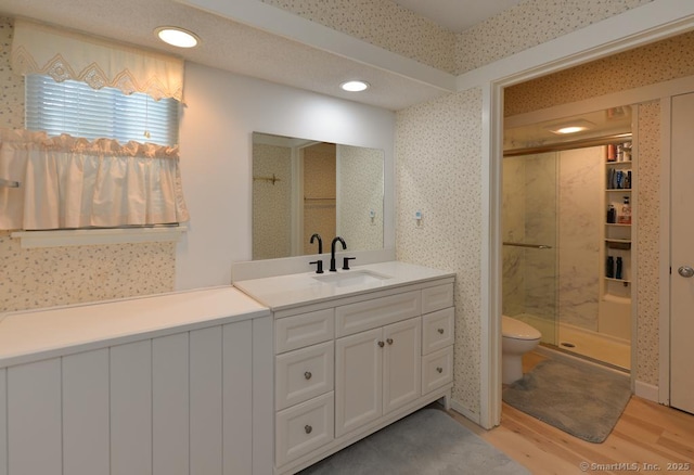 bathroom with a shower stall, wallpapered walls, toilet, wood finished floors, and vanity